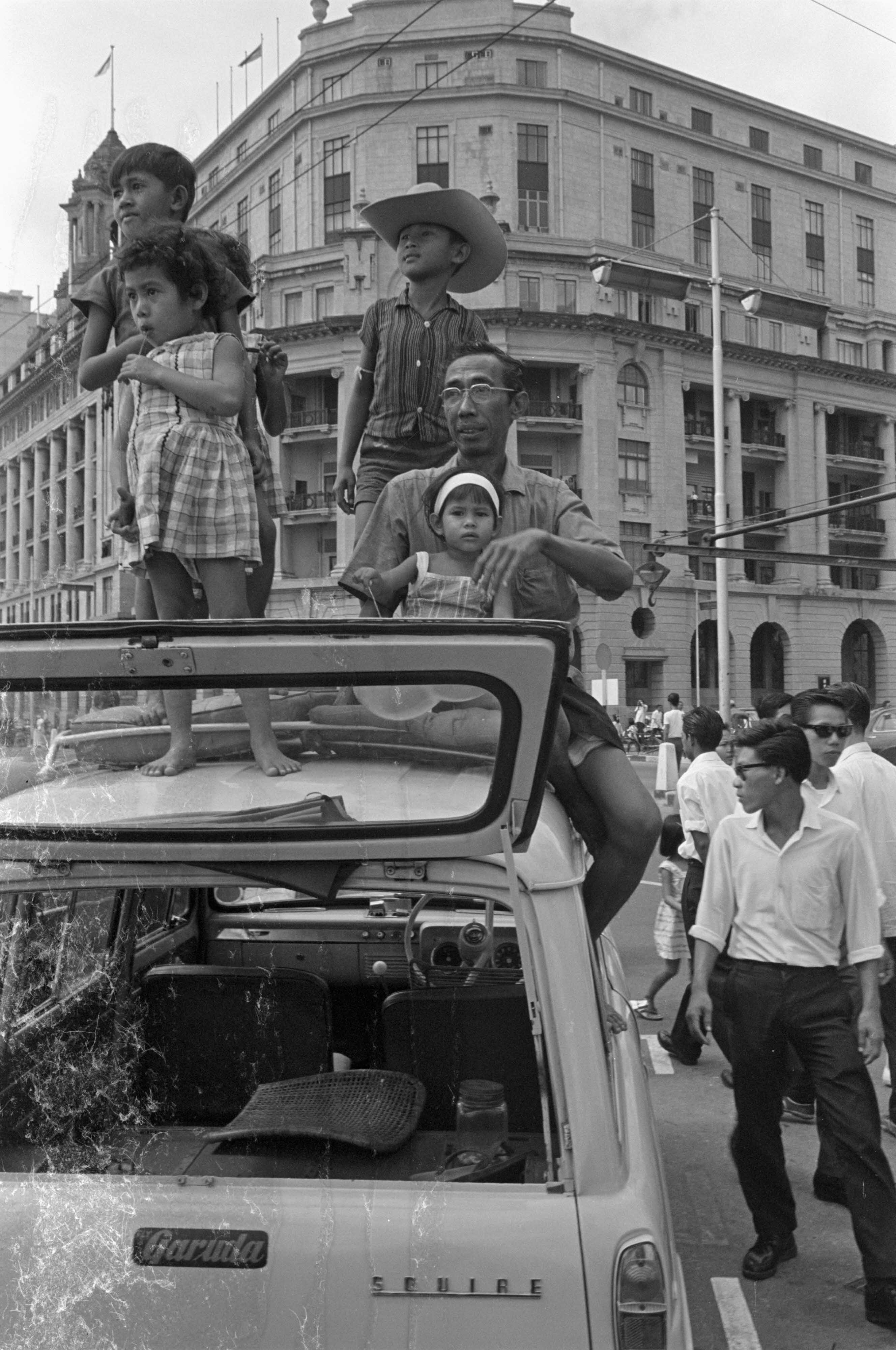 A family perches on the top of their car, eager to catch a glimpse of the New Year Sea Sports, 1963.